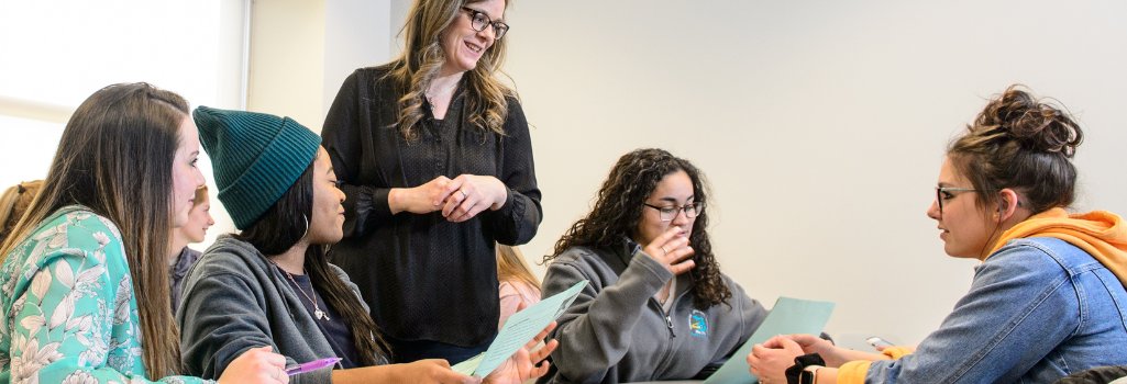 A group of 4 students and 1 teacher conversing at a table.